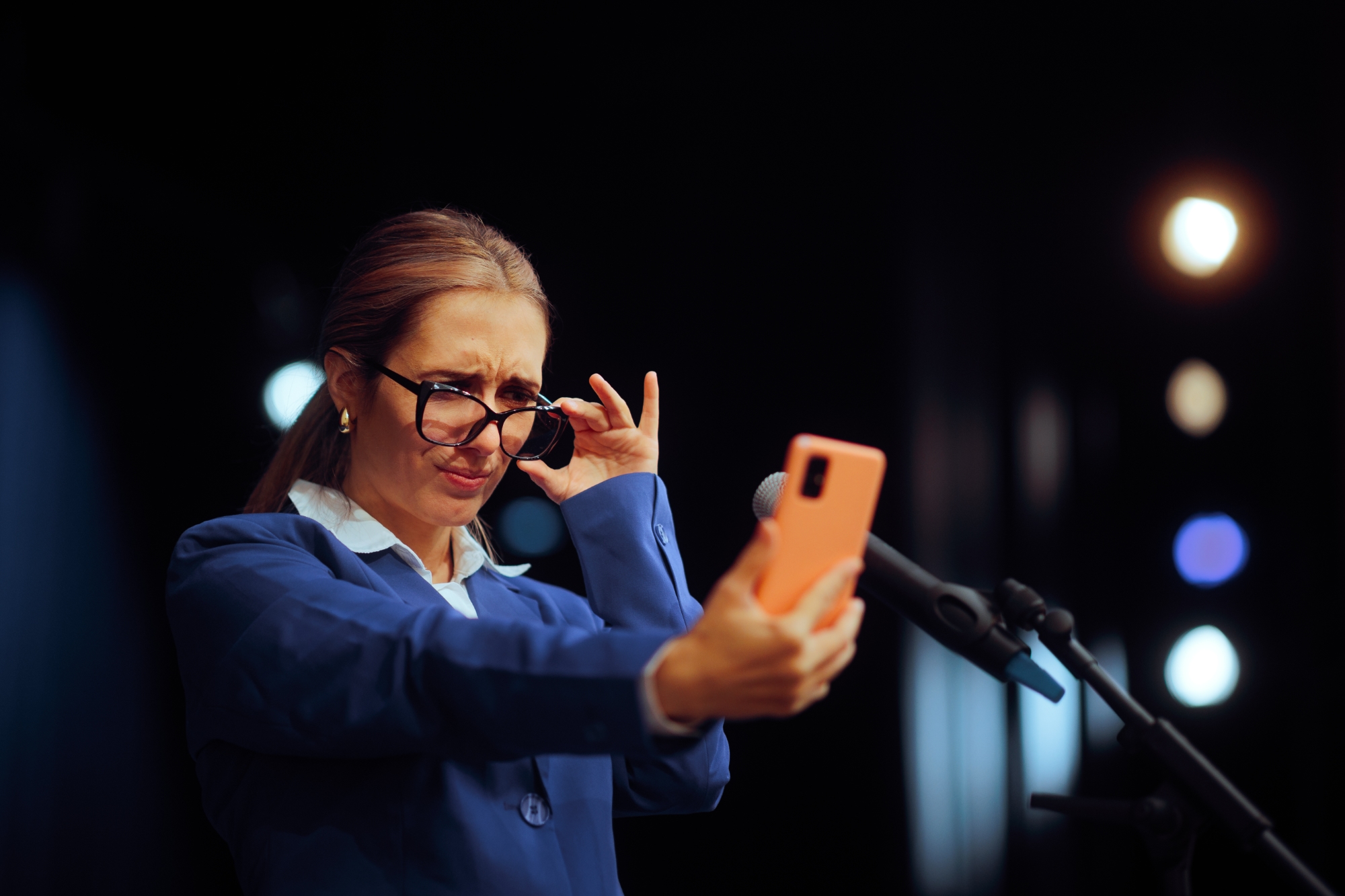 Alterssichtigkeit bei kurzssichtiger Frau, die ihre Brille hochh&auml;lt, um auf das Smartphone zu schauen.