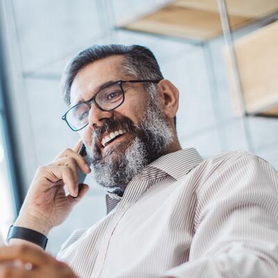 Mann im Büro mit Gleitsichtbrille schaut sich Unterlagen an, während der telefoniert.