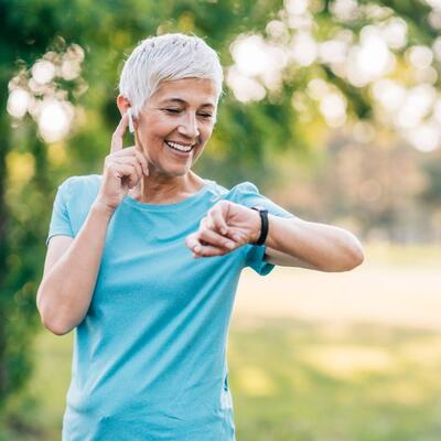 Frau mittleren Alters draußen beim Sport schaut auf ihre Smartwatch.