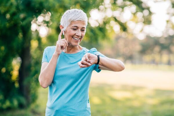Frau mittleren Alters draußen beim Sport schaut auf ihre Smartwatch.