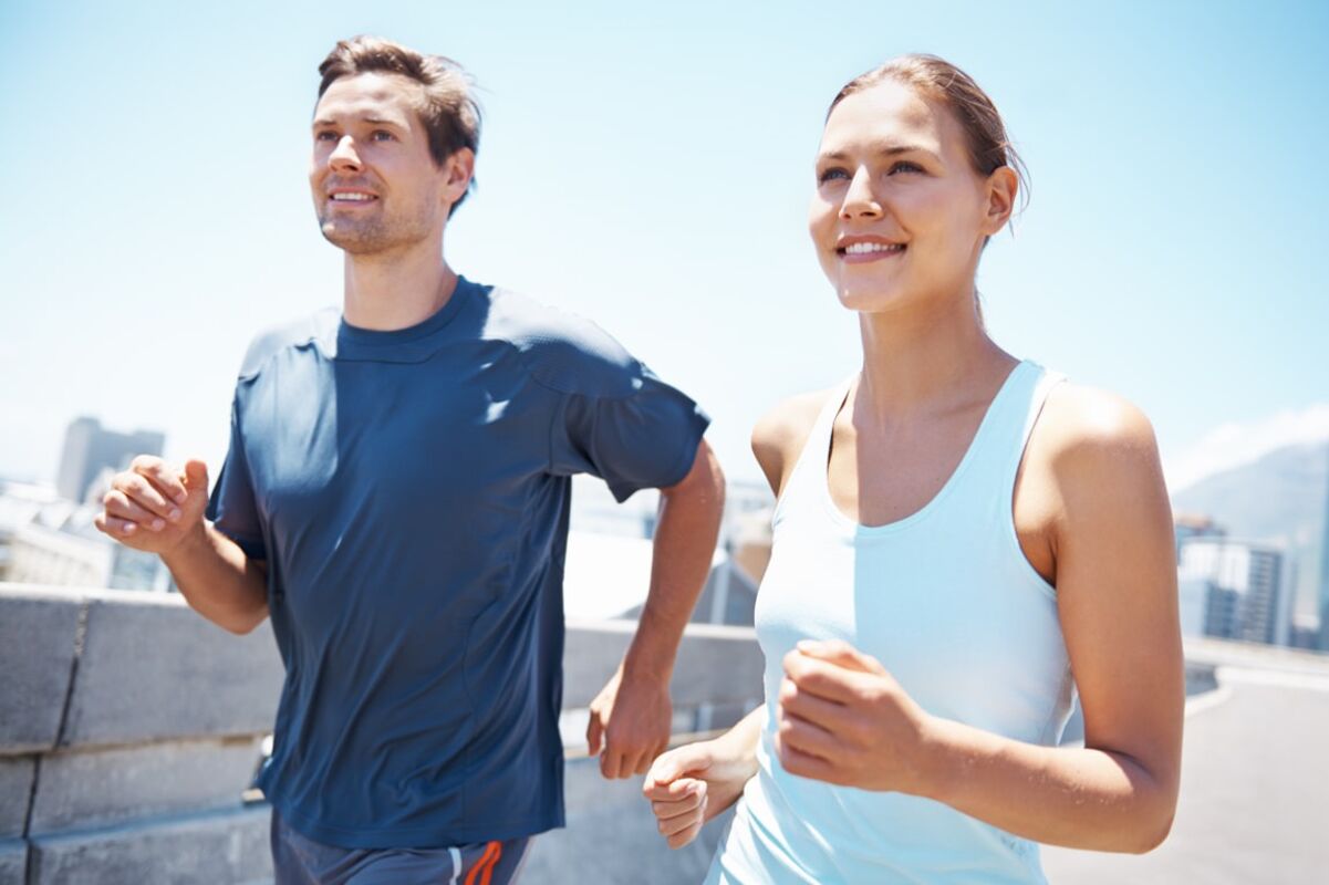 Ein junger Mann und eine junge Frau joggen über eine Brücke, im Hintergrund ist eine Großstadt zu erkennen.