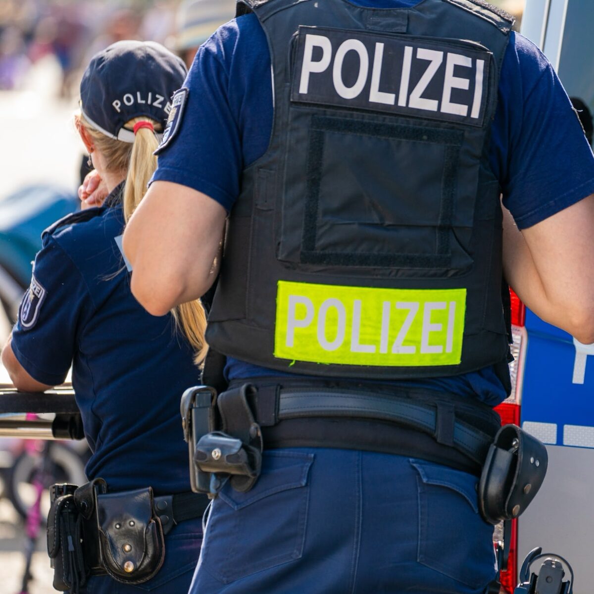 Close-up auf ein blaues Polizeiauto, im Hintergrund sind Polizisten zu sehen.
