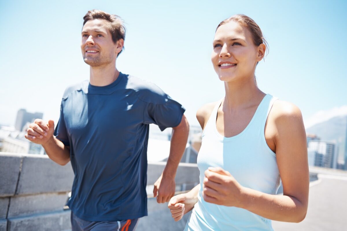 Ein junger Mann und eine junge Frau joggen über eine Brücke, im Hintergrund ist eine Großstadt zu erkennen.
