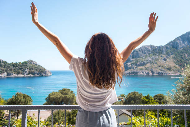 Frau steht morgens auf der Terrasse und schaut aufs Meer.