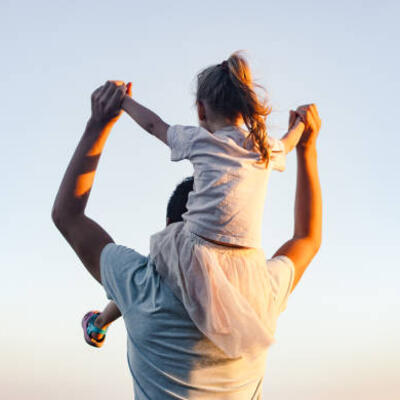 Ein Vater mit seiner Tochter auf seinen Schultern blickt in die Ferne.