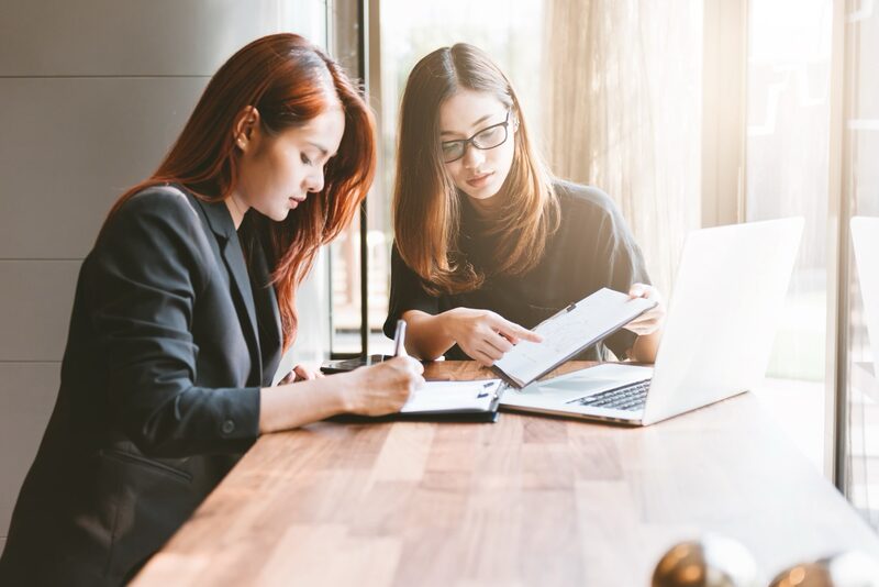 Zwei asiatische Frauen arbeiten gemeinsam am Laptop.