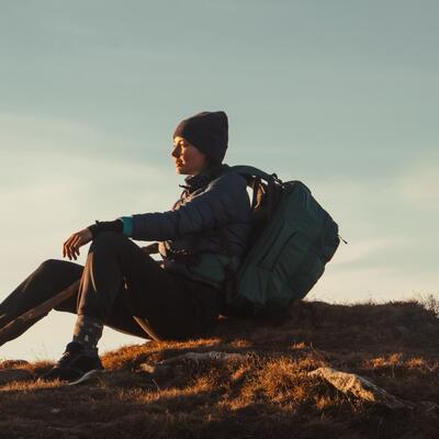 Junge Frau mit Rucksack ruht sich auf einem Berggipfel aus.