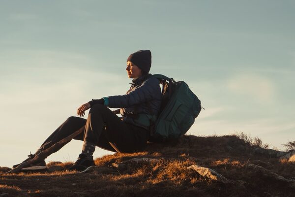 Junge Frau mit Rucksack ruht sich auf einem Berggipfel aus.