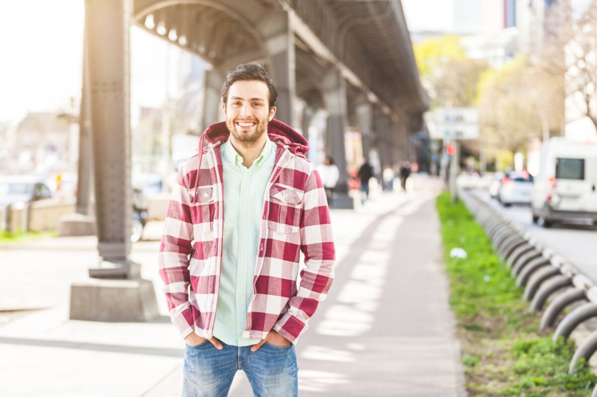 Junger Mann in karierter Jacke steht unter einer Brücke in der Stadt.