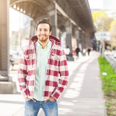 Junger Mann in karierter Jacke steht unter einer Brücke in der Stadt.