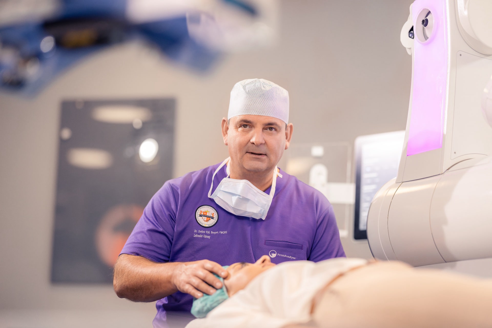 Dr. Breyer sitzt am Visumax und erklärt einer Patientin, die auf der OP-Liege liegt, den Ablauf der Behandlung.