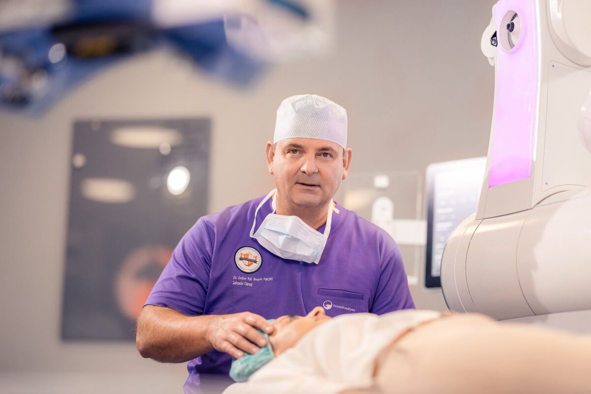 Dr. Breyer sitzt am Visumax und erklärt einer Patientin, die auf der OP-Liege liegt, den Ablauf der Behandlung.