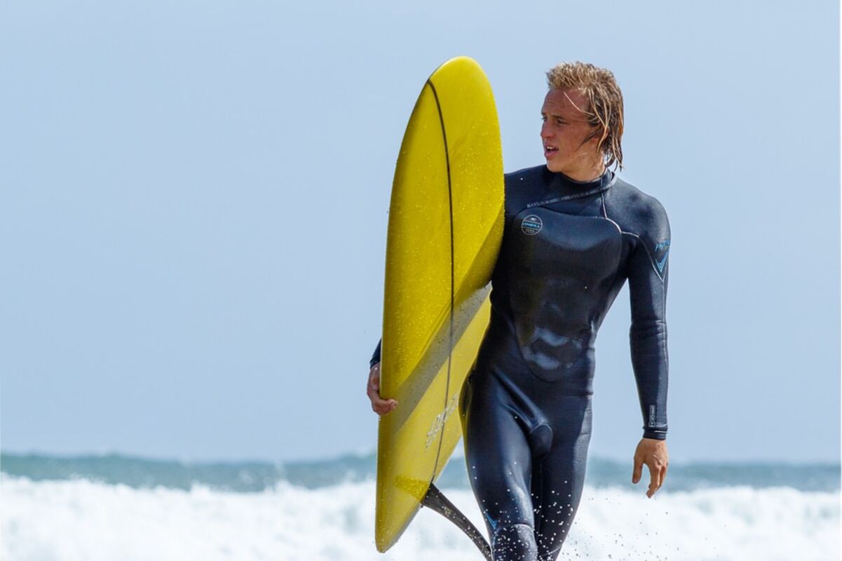 Surfer mit Surfbrett geht durch das Wasser an den Strand.