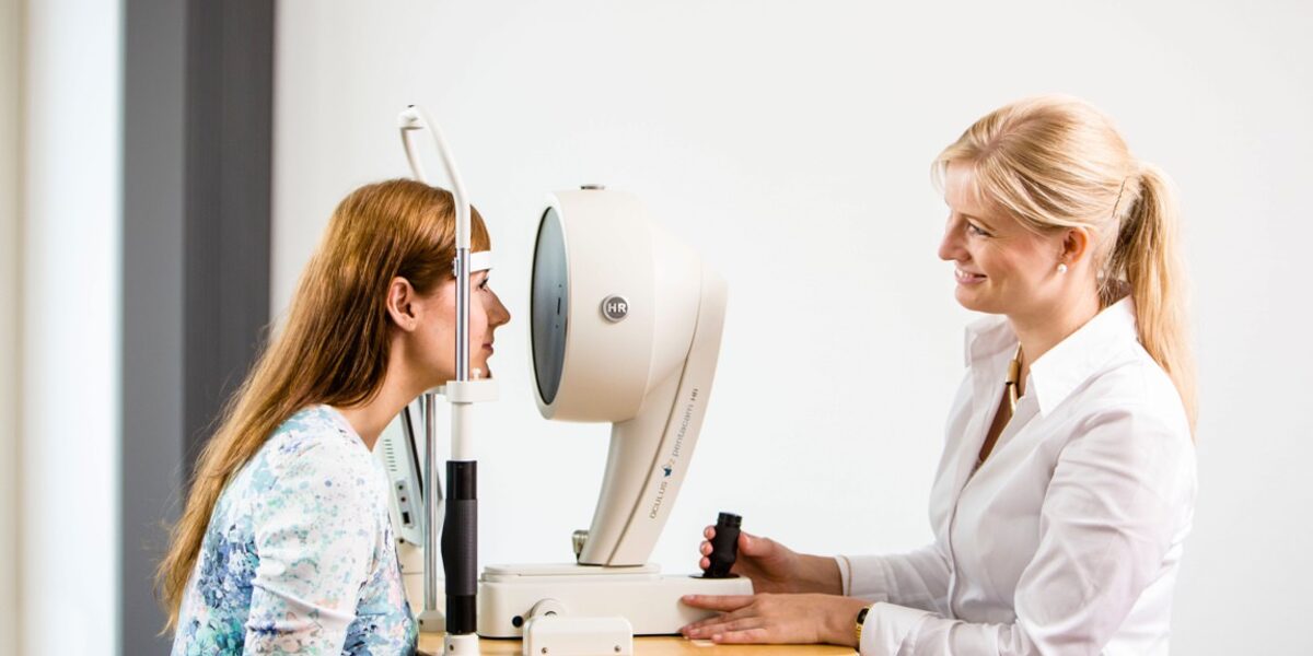 Eine Mitarbeiterin der Praxisu untersucht die Augen einer jungen Frau mit der Pentacam HR.