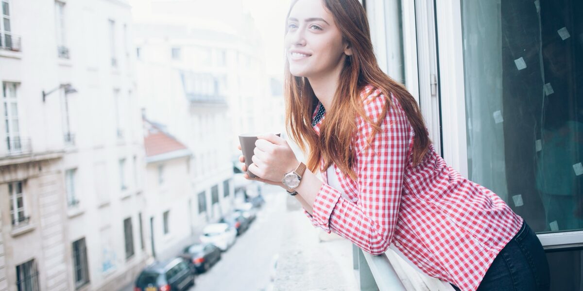 Junge Frau mit einer Tasse Kaffee blickt entspannt aus dem Fenster.