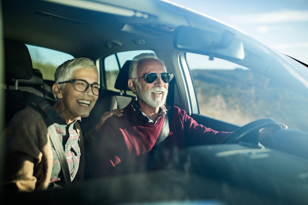 Senior-Paar fährt im Auto durch eine Landschaft.