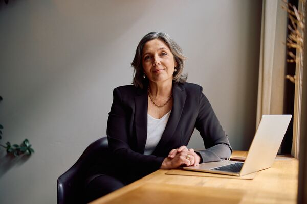 Frau mittleren Alters am Computer blickt in die Kamera.