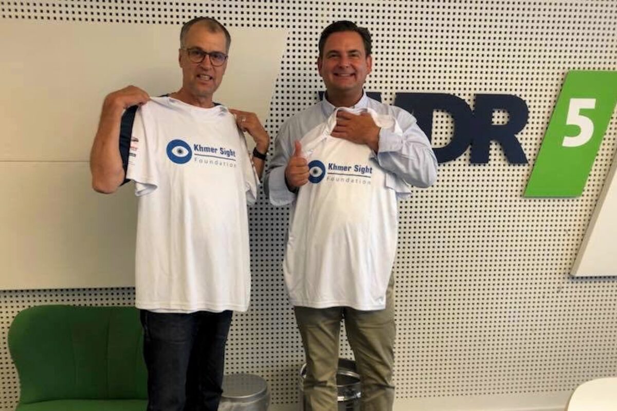 Thomas Koch und Dr. Breyer halten Shirts mit dem Logo der Khmer Sight Foundation hoch.