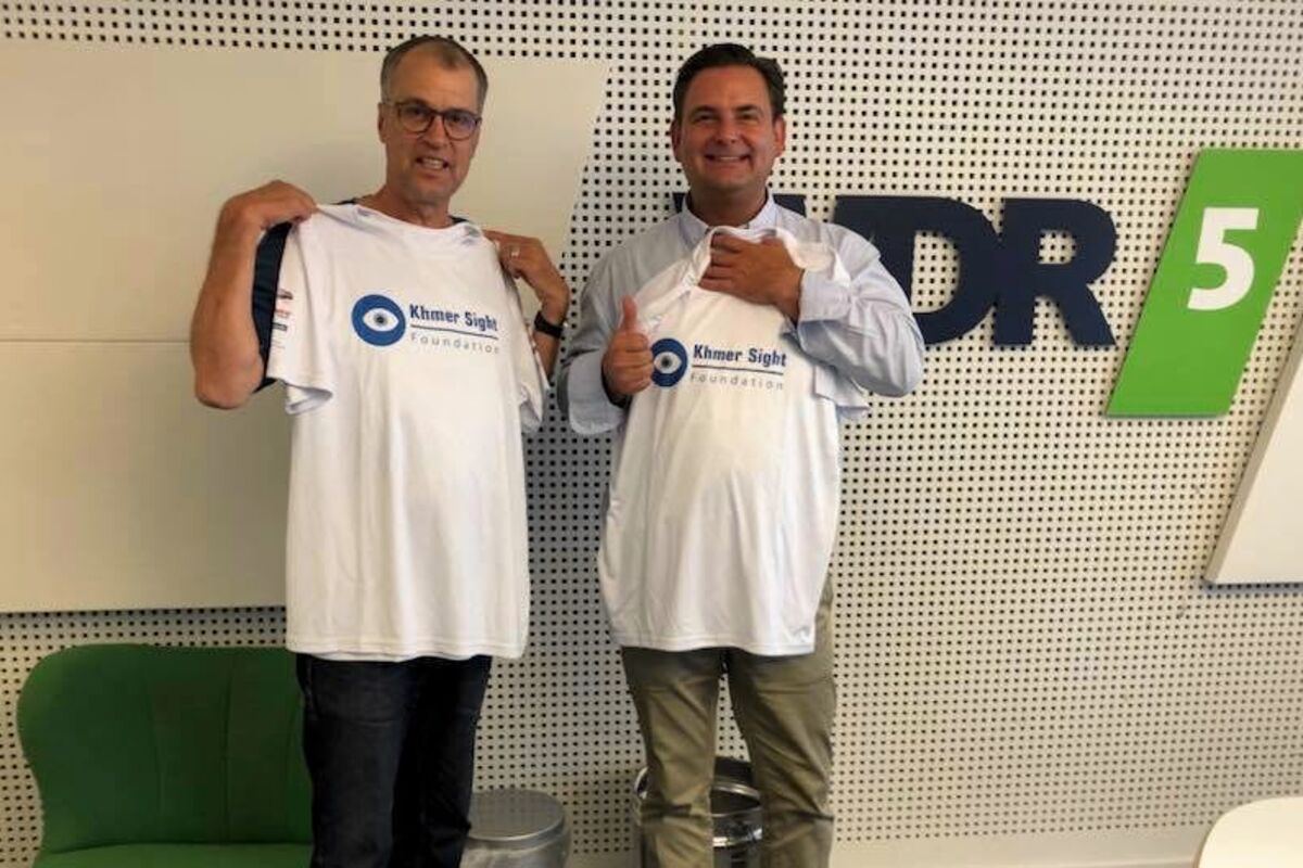  Thomas Koch und Dr. Breyer halten Shirts mit dem Logo der Khmer Sight Foundation hoch.